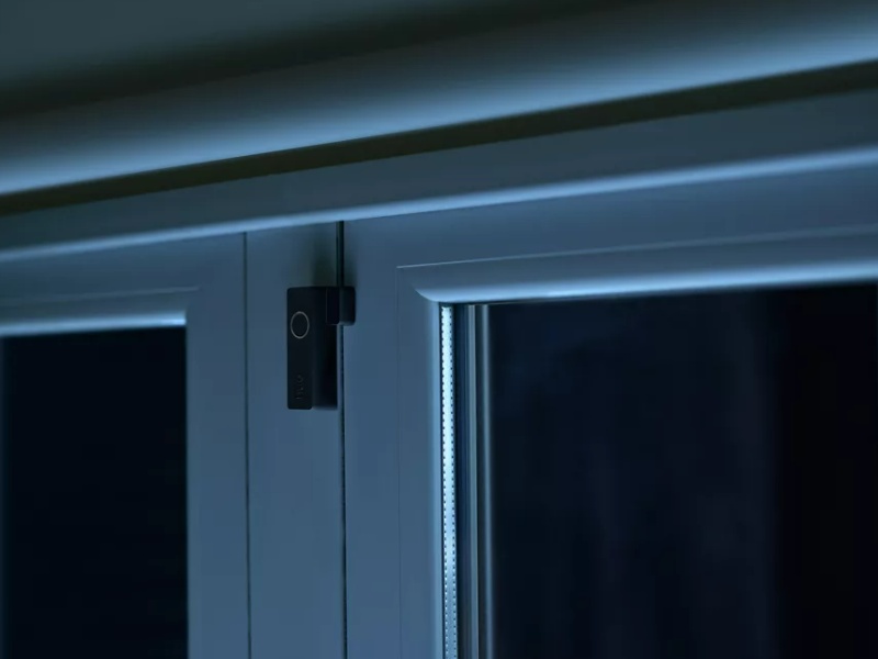 Slimme deur-/raamsensor op wit kozijn in donkere kamer, een van de '5 Slimme 'Hacks' voor je Deur-/Raamsensor'.