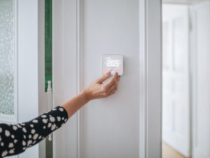 Hand past een slimme thermostaat aan op een witte muur.