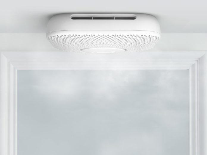 Een witte rook- en koolmonoxidemelder (Nest Protect) hangt aan een wit plafond boven een deuropening met een witte lijst.