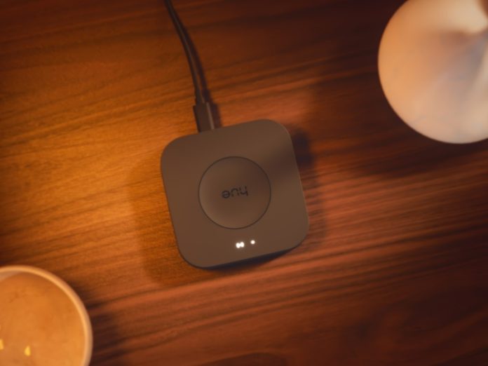 Donkergrijze Philips Hue Bridge Pro aangesloten met een kabel op een houten tafel, met twee witte statuslampjes aan.