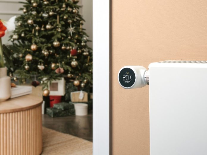 Witte Slimme Thermostaat op radiator toont 20.5°C, met een kerstboom in een sfeervolle woonkamer op de achtergrond.