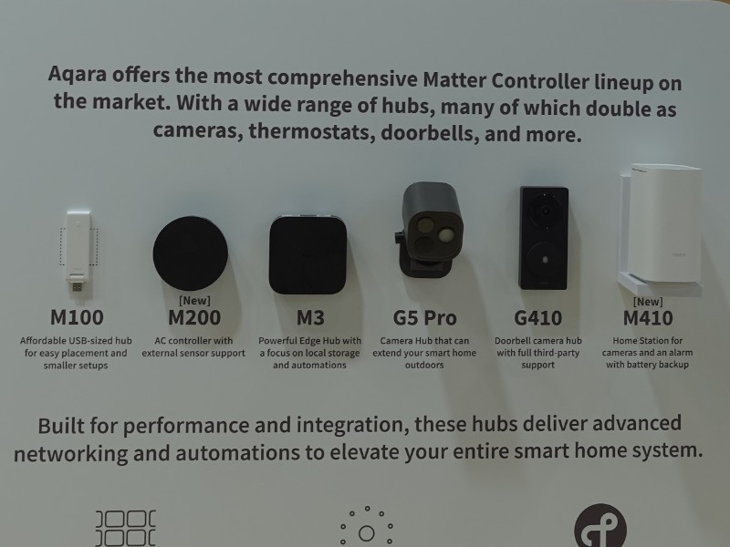 Overzicht van Aqara Matter Controllers op een display, met zes verschillende hubs. Centraal staat de nieuwe, zwarte, ronde Aqara Hub M200, samen met vijf andere modellen. Het witte paneel met titels in wit en roodbruin staat op een houten achtergrond.