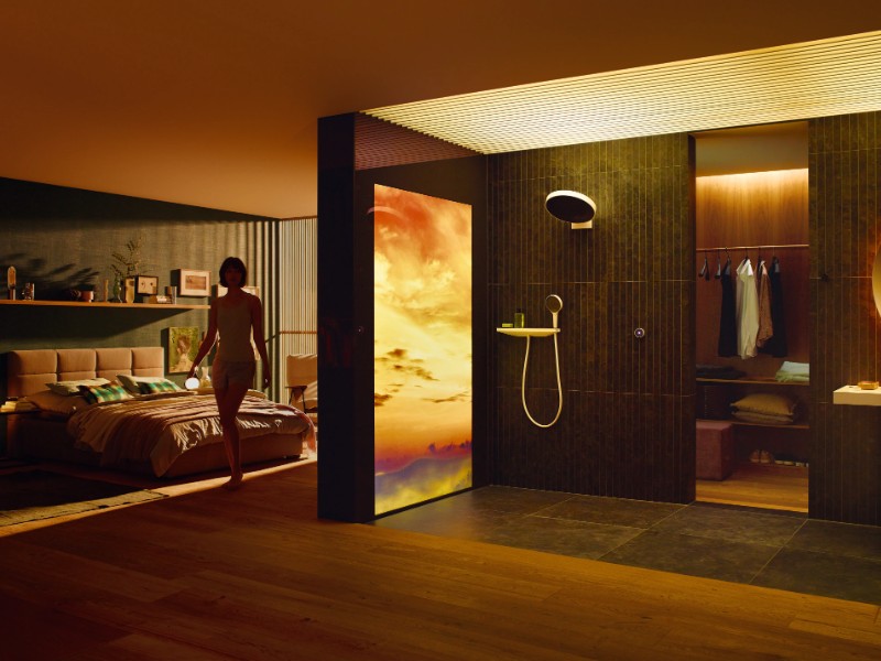 Een sfeervol interieur met warme verlichting, waar een vrouw langs een lichtpaneel met een levendige oranje-paarse zonsondergang loopt, wat de overgang naar de donkerdere avonden na het Einde zomertijd accentueert en begin wintertijd.