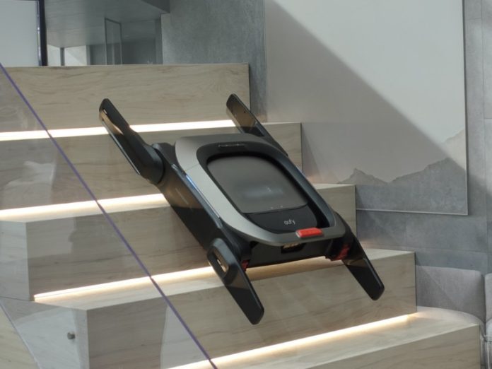 Donkergrijze Eufy Marswalker met zilveren accenten en rode knop, schuin geplaatst op een verlichte houten trap.