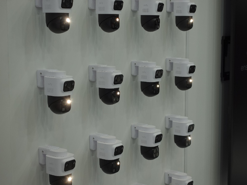 Rijen witte EufyCam S4 bewakingscamera's, elk met een zwart roterend onderdeel en 'eufy' logo, hangen op een witte muur; sommige stralen een fel wit licht uit.