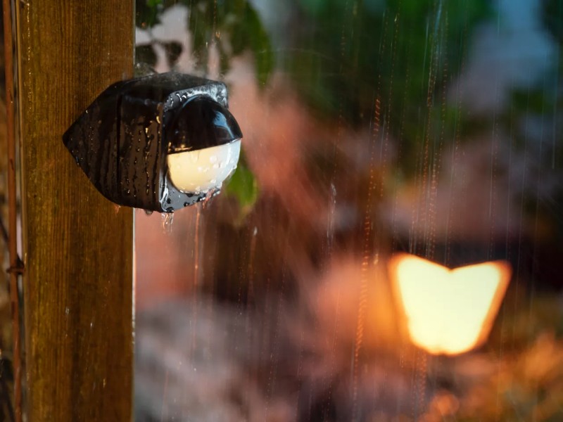 Een zwarte en witte  hue buitenlamp  met regendruppels, gemonteerd op een houten paal, illustreert de IP-waarde.