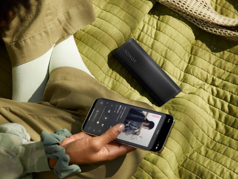 Zwarte draagbare Sonos speaker en smartphone op een groene deken, die de veelzijdigheid van een Toekomstbestendig smarthome toont.