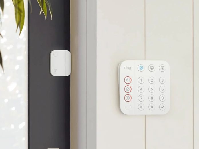 Wit Ring Alarm Systeem bedieningspaneel met numeriek toetsenbord en een witte deursensor op een donkergrijs deurkozijn, naast een crèmekleurige wand.