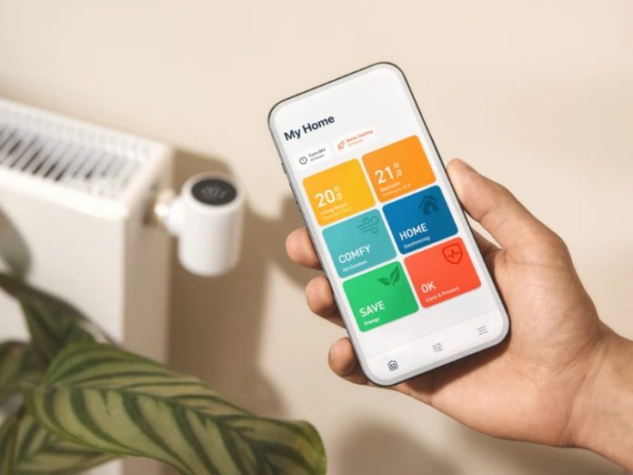 Een hand toont de tado app op een witte smartphone, met kleurrijke tegels in geel, oranje, lichtblauw, donkerblauw, groen en rood die temperaturen en functies weergeven. Op de achtergrond staat een witte radiator met een tado thermostaat, naast een groene plant en een beige muur.