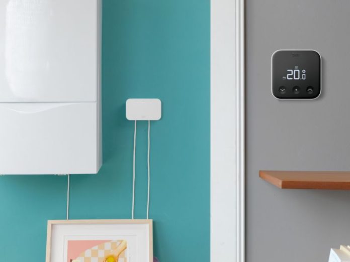 Witte tado-internetbridge en cv-ketel op een blauwgroene muur, met een zwarte tado-thermostaat op een grijze muur die een temperatuur van 20,0 graden weergeeft.