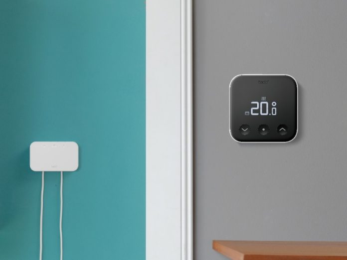 Witte verwarmingsketel en tado Bridge met kabels op turquoise muur, naast een zwarte tado slimme thermostaat (20.0°) op grijze muur met houten plank.