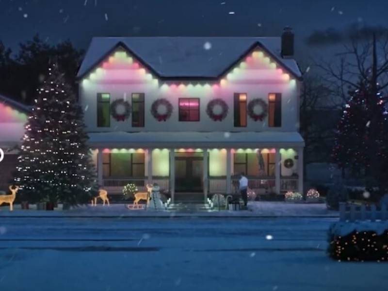 Feestelijk verlicht wit huis met kleurrijke kerstverlichting (roze, groen) en lichtgevende rendieren in de sneeuw, wat herinnert aan het belang van Huis beveiligen feestdagen.