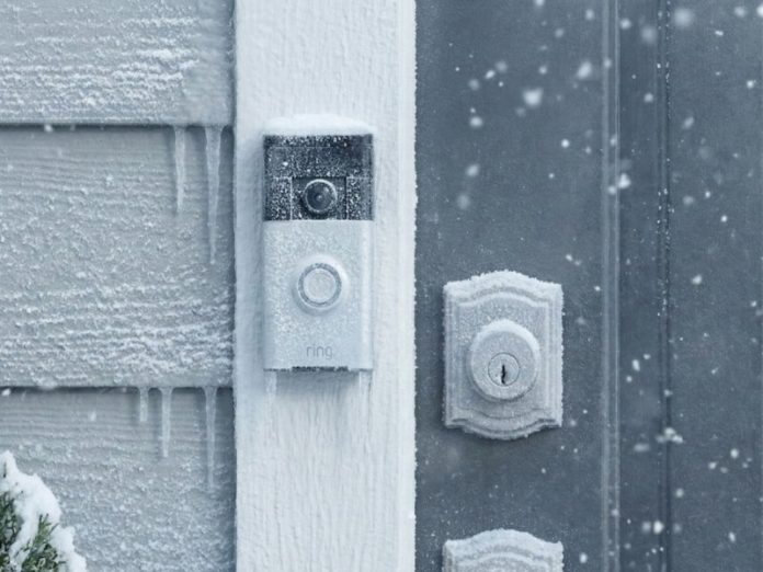 Een witte slimme deurbel van Ring, zwaar bevroren op een grijsblauwe muur met ijspegels. De winterse omstandigheden benadrukken de uitdaging van Slimme deurbel batterij kou.