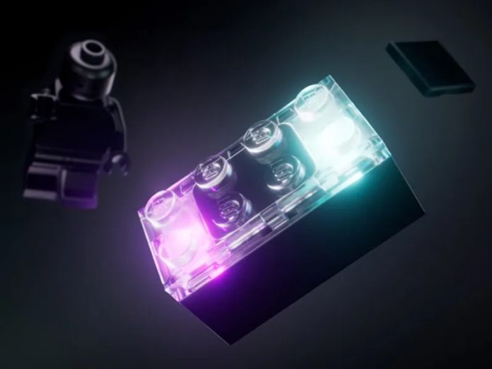 Doorschijnende LEGO Smart Brick in paarse en cyaan gloed, zwevend in een donkere ruimte naast een zwarte LEGO minifiguur.