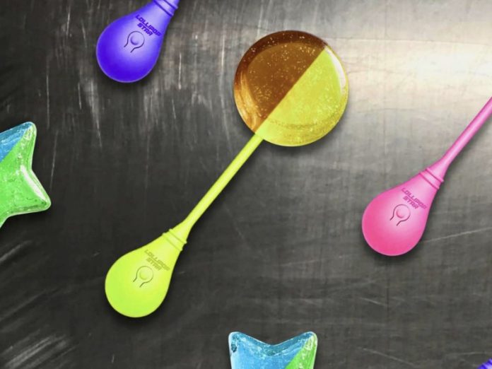 Verspreide tweekleurige 'Lollipop Star' lolly's met lichtbolvormige handvatten, waaronder een ronde geel-bruine en een blauw-groene ster, op een donkergrijze ondergrond (CES 2026).