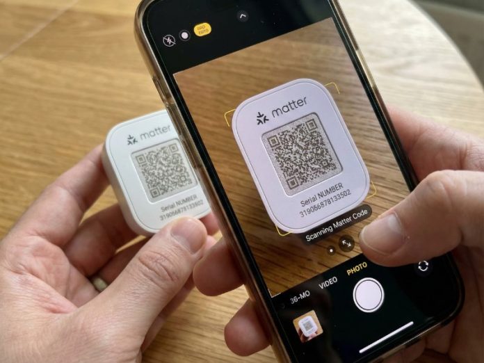 Handen scannen de QR-code op een wit Matter-apparaat met een smartphone voor Matter installeren. Het Matter-logo en serienummer zijn zichtbaar op het scherm.