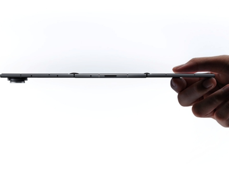 Zijprofiel van de ultradunne, donkergrijze Samsung Galaxy Z TriFold, volledig uitgevouwen en vastgehouden door een hand, met nadruk op de scharnieren en de prominente ronde cameramodule.