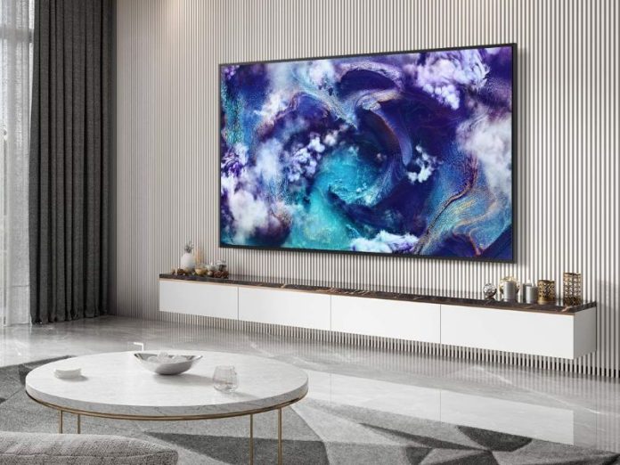 Grote Samsung TV SmartThings Hub aan een witte lattenmuur, met levendige blauw-paarse en gouden abstracte kunst. De tv hangt boven een wit zwevend dressoir in een moderne, lichte woonkamer.