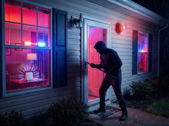 Een inbreker probeert een huis binnen te dringen op een regenachtige nacht, terwijl de SmartThings Home Monitor alarmlichten (fel rood en blauw) en de buitensirene afgaan.