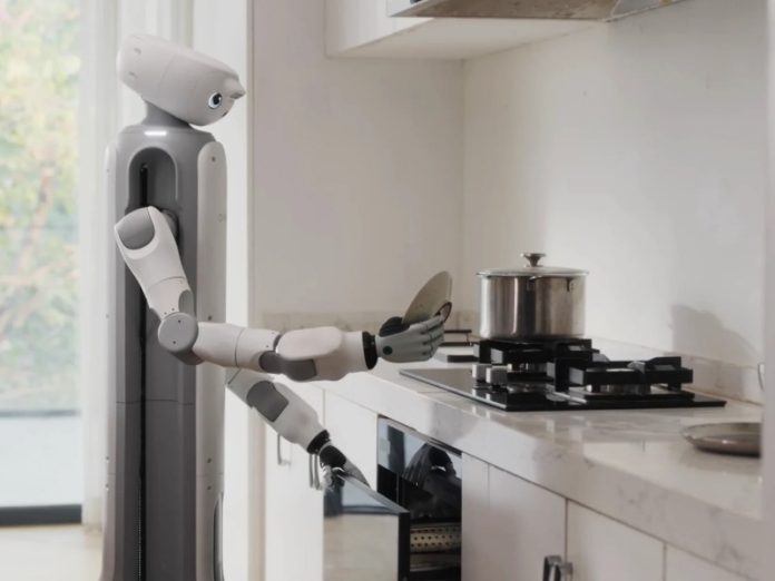 De SwitchBot onero H1 robot butler, grijs en wit, staat in een lichte keuken met marmeren aanrecht, een spatel en mes vasthoudend naast het fornuis.