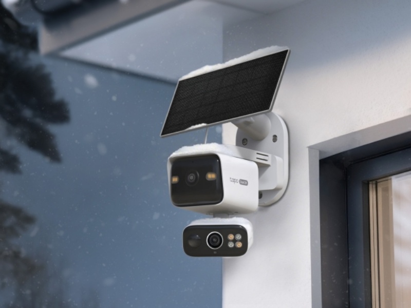 Witte TP-Link Tapo AI-beveiligingscamera met een zwart zonnepaneel, bedekt met lichte sneeuw, gemonteerd op een buitenmuur. Het IP65 water- en stofbestendige systeem functioneert tijdens zware winterse neerslag.