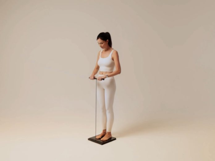 Slanke vrouw in witte sportkleding gebruikt de donkergrijze Withings Body Scan 2 op een lichte beige achtergrond.