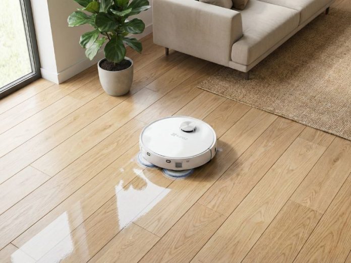 Een witte EZVIZ robotstofzuiger met zilveren accenten en blauwe dweilpads dweilt een lichte houten vloer, met zichtbare natte sporen. Dit illustreert 