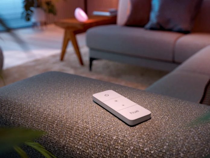 Witte Philips Hue afstandsbediening, een slimme schakelaar die mogelijk dient als een google home matter knop, rustend op een gestoffeerde bankleuning.