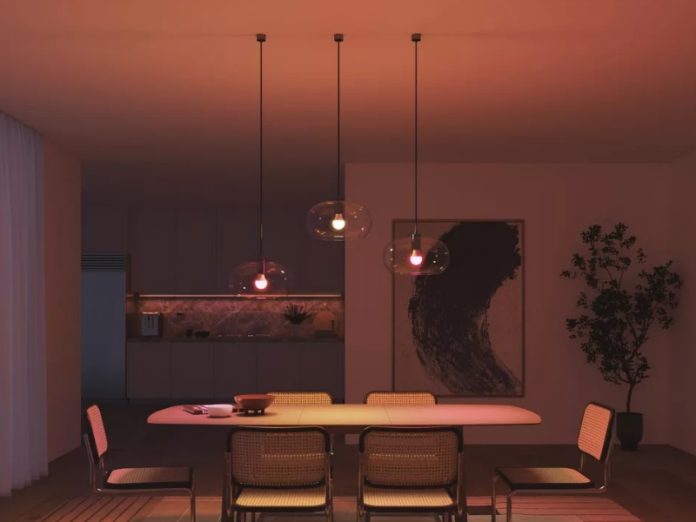 Sfeervolle moderne eetkamer met drie glazen hanglampen die een warme, rode hue uitstralen over de eettafel en rieten stoelen.