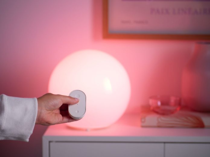 Hand met witte afstandsbediening bedient een bolvormige Ikea lamp die felroze/magenta licht uitstraalt.