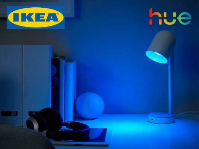 Witte IKEA Kajplats Philips Hue bureaulamp die fel blauw licht uitstraalt over een bureau met boeken en koptelefoon.