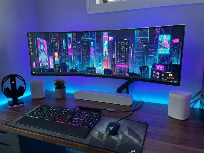 Futuristische pc-opstelling met ultrabrede, gebogen monitor met neon-cyberpunk stadsgezicht. De houten desk is verlicht met blauwe/paarse ambient verlichting. Drie witte Sonos luidsprekers (een soundbar en twee kleine speakers) staan op het bureau, passend bij het onderwerp Sonos aansluiten op je PC.