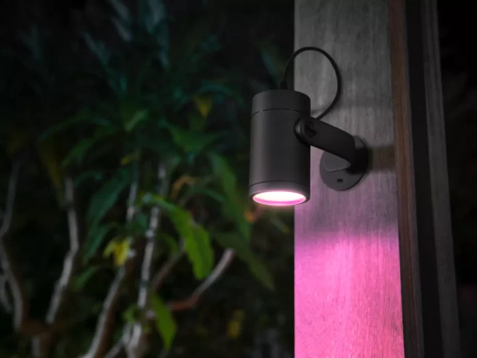 Zwarte Philips Hue buitenlamp die een fel roze licht werpt op een grijze houten paal in een donkere tuin; zijn je Philips Hue buitenlampen offline?