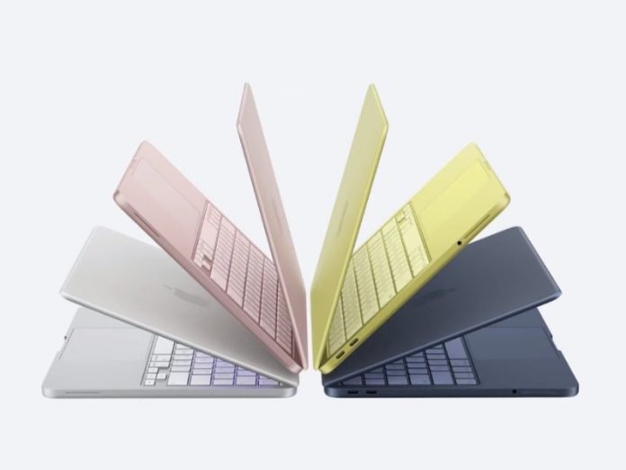 Vier geopende MacBook Neo laptops in zilver, roze, geel en donkerblauw, met de toetsenborden naar elkaar gericht.