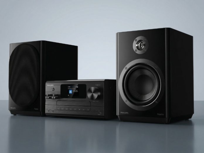 Philips Fidelio FA7 & L5 onthuld: een strakke zwarte hifi-set met een centrale unit van geborsteld metaal en twee bijpassende luidsprekers op een reflecterende grijze ondergrond.