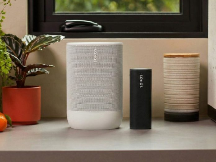 Twee Sonos-speakers, een grote witte en een kleinere zwarte, op een grijze ondergrond, omringd door groene planten, mandarijnen en keukenelementen, mogelijk ter vergelijking van Sonos-producten.