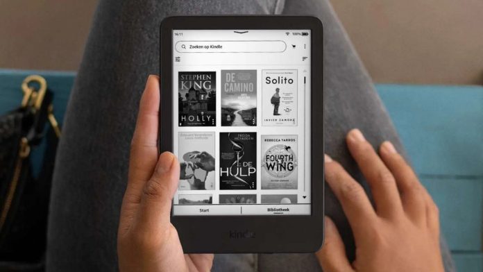 Iemand in een grijze spijkerbroek houdt een zwarte Amazon Kindle e-reader vast. Het scherm toont een digitale bibliotheek vergelijkbaar met de Amazon Kindle app op een PC, met diverse boekcovers in zwart-wit. Witte tekst bovenaan benadrukt dat de Kindle licht en compact is met verbeterde schermfuncties. Op de achtergrond zijn een blauwe zitting en een zwarte handtas met gouden details zichtbaar.
