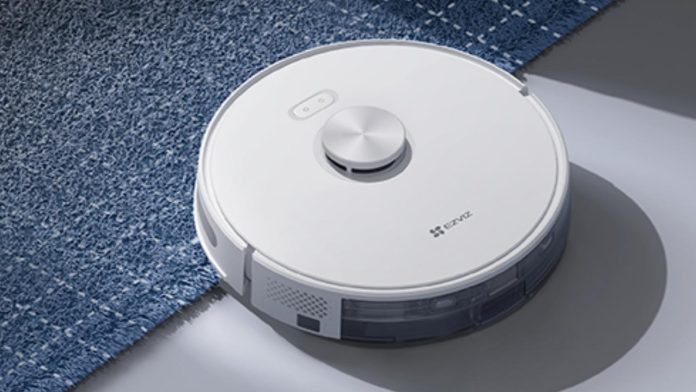 Een witte EZVIZ robotstofzuiger rijdt van een gladde grijze vloer op een blauw hoogpolig tapijt, gepresenteerd als de beste robotstofzuiger voor jouw vloertype (2026).
