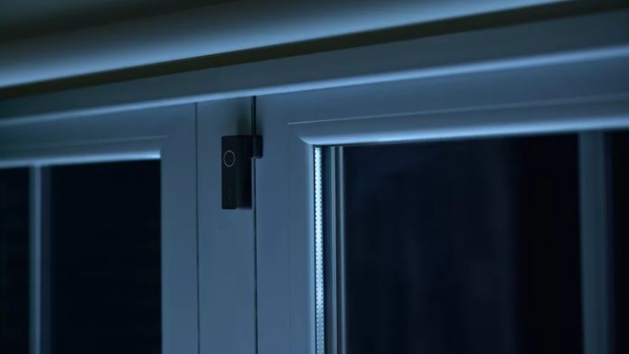 Een zwarte Philips Hue contactsensor gemonteerd op een wit raamkozijn in een sfeervol, blauwachtig verlichte kamer, ideaal voor Hue contactsensor automatiseringen.