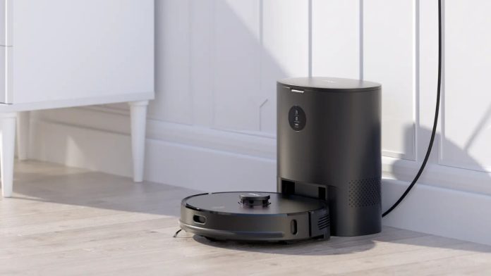 Zwarte robotstofzuiger bij een bijpassend laadstation op een lichte houten vloer in een modern wit interieur, een effectieve robotstofzuiger allergie oplossing.