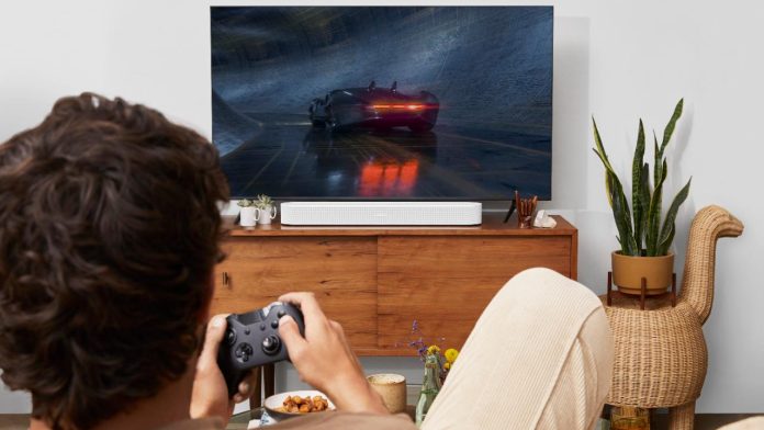 Een persoon speelt een racegame op een televisie met een witte Sonos soundbar op een houten dressoir, een scenario waarin Sonos audio lag merkbaar kan zijn.