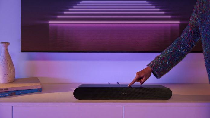Een vinger drukt op de knop van een zwarte Sonos soundbar onder een tv met paarse neonverlichting om de Sonos te verbinden met een nieuwe router.