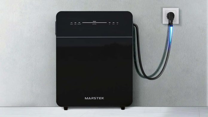 Zwarte Marstek stekkerbatterij aangesloten op een stopcontact in een lichtgrijze muur met een blauw oplichtende kabel.