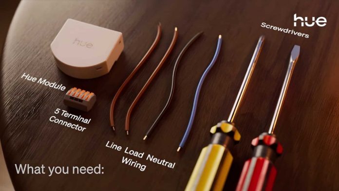 Een overzicht van de installatiebenodigdheden op een houten tafel, waaronder de witte Hue Wall Switch Module, een 5-polige lasklem, elektriciteitsdraden en schroevendraaiers.