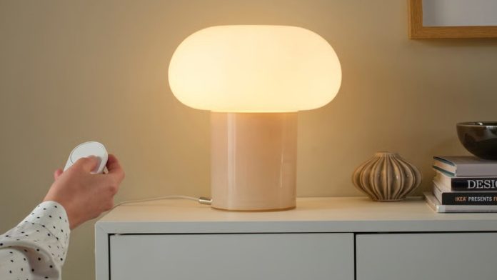 Een paddenstoelvormige IKEA Bilresa tafellamp met een witte glazen kap en een beige voet op een wit dressoir, die een warm geel licht uitstraalt.