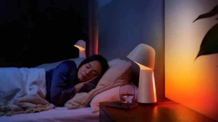 Slapende vrouw in een donkere kamer met een smart home lamp die een warme oranje-gele gloed op de muur werpt, passend bij het thema nachtdienst & smart home.