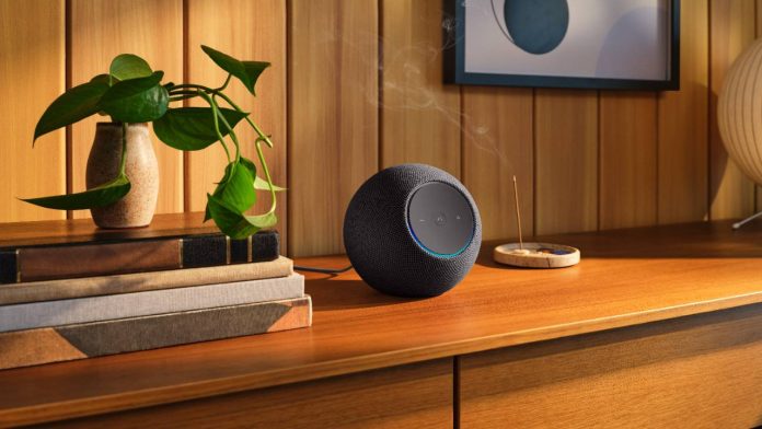 Een donkergrijze, ronde smart home hub op een houten dressoir naast een stapel boeken en een groene plant, wat de situatie illustreert van een Smart Home Hub Offline In Het Buitenland in een sfeervol interieur.