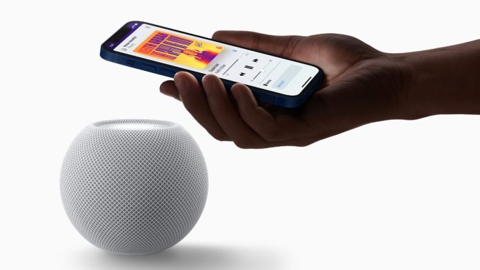 Hand met een blauwe iPhone boven een witte HomePod mini om muziek over te dragen via Apple Home.