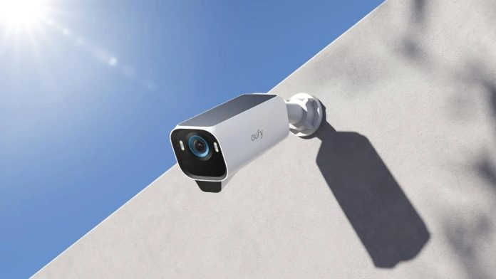 Witte Eufy beveiligingscamera met een blauwgerande lens gemonteerd op een witte muur in de felle zon onder een strakblauwe hemel; een treffend voorbeeld van buitengadgets beschermen hitte.