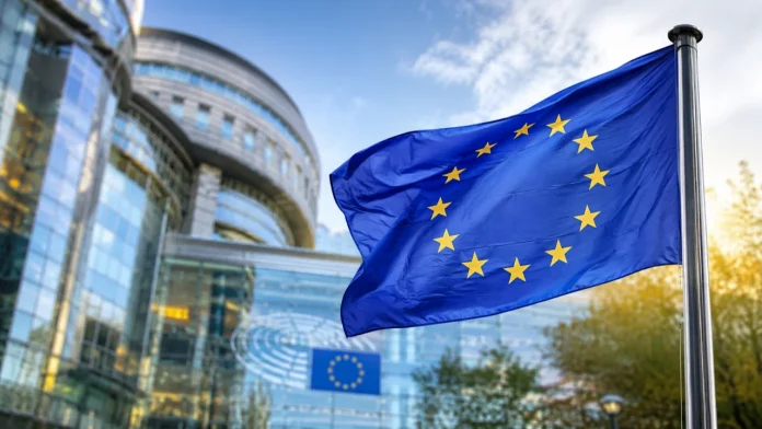 De vlag van de Europese Unie wappert voor een modern glazen parlementsgebouw in Europe onder een helderblauwe lucht.